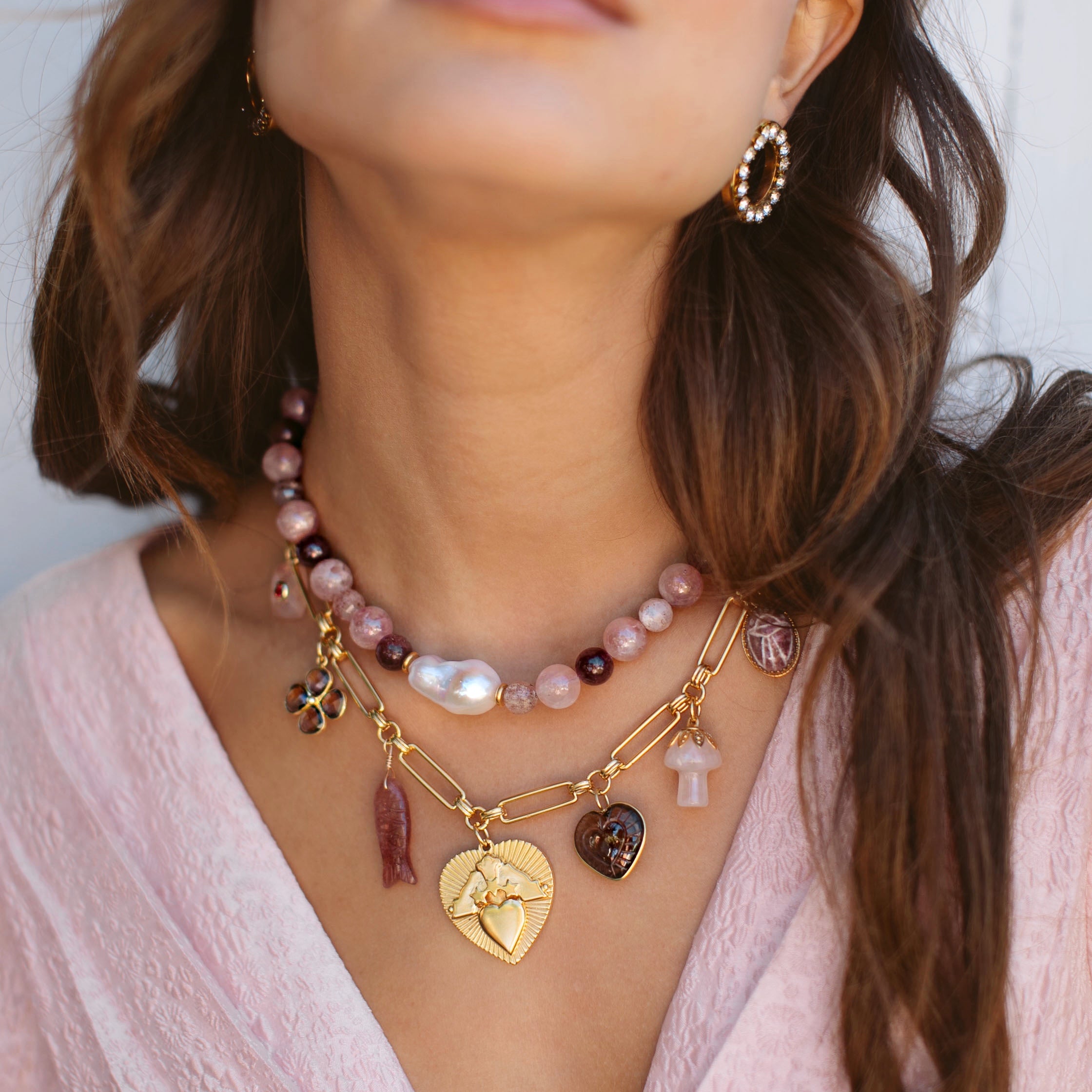 Woman wearing multiple necklaces with heart and flower charms, against a neutral background