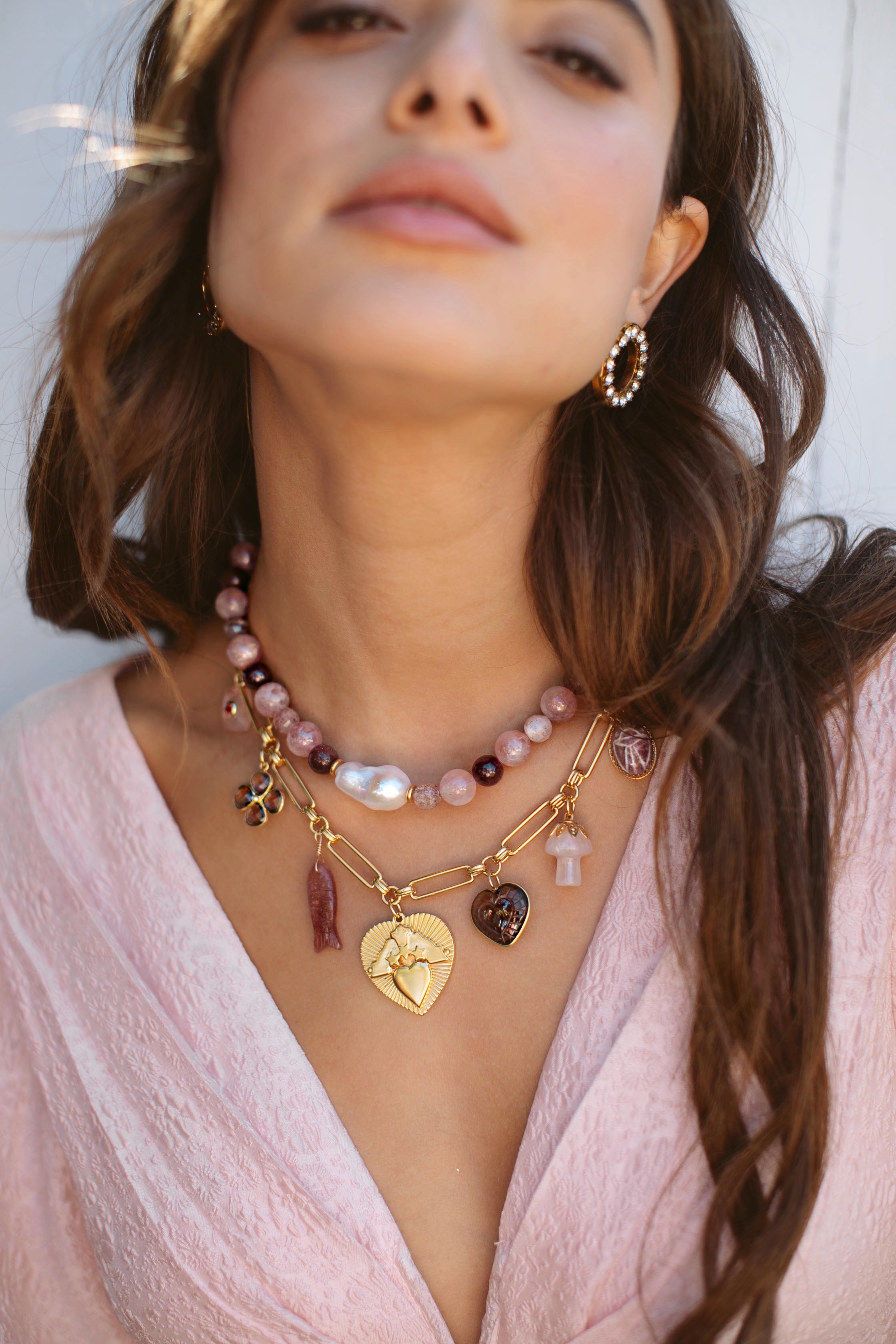 Woman wearing multiple necklaces with heart and flower charms, against a neutral background